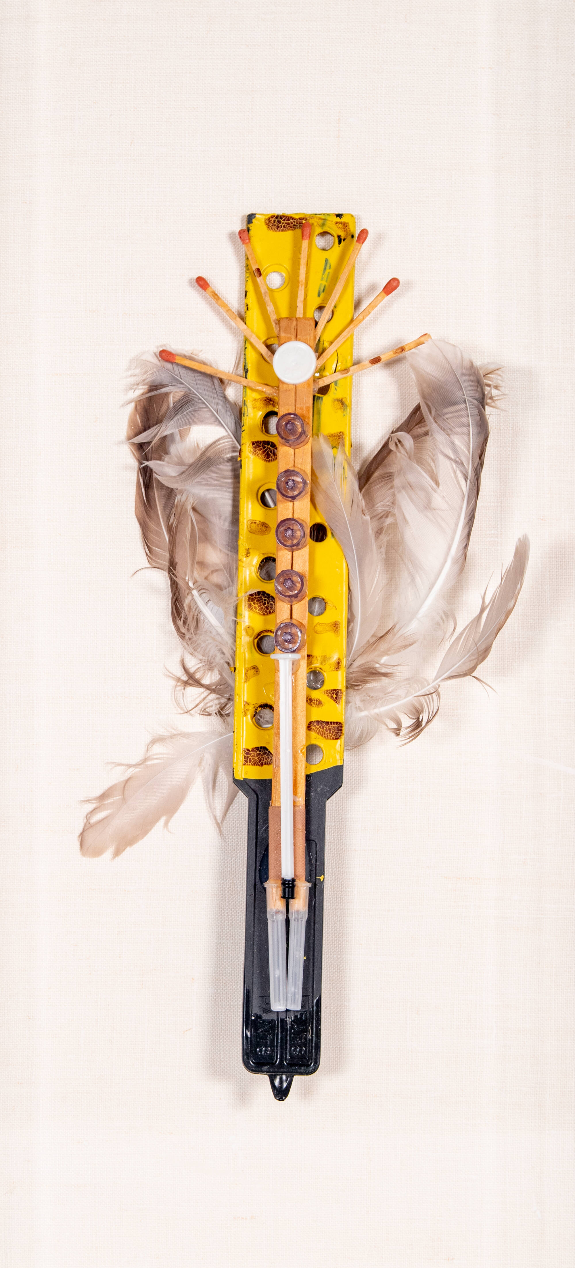 Mixed media sculpture that looks like a stick with feather rings.